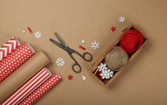 Close up packing and wrapping Christmas gifts with red and brown paper, table top view, flat lay