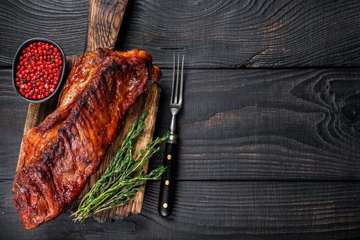 Grilled in bbq sauce veal short spare rib meat on wooden cutting board. Black wooden background. Top view. Copy space.