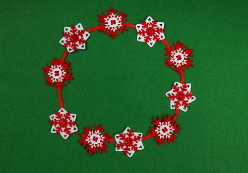 Close up circle of red and white snowflake shaped Christmas decoration garland over green felt background with copy space, table top view, flat lay