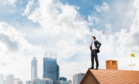 Young determined businessman standing on house roof and looking away. Mixed media