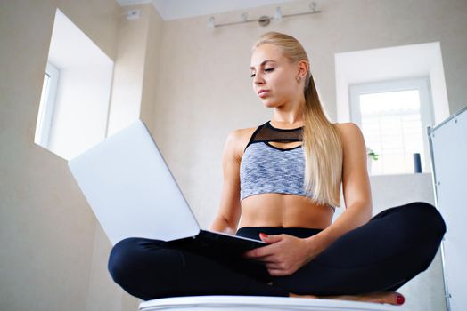 Sports business girl with laptop in lotus pose looks at laptop shot from the bottom