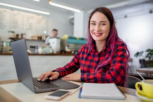 Young woman with pink hair with laptop computer sitting in cafe, intelligent female student working on net-book after her lectures in University