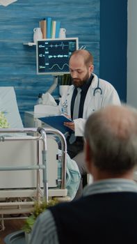 Doctor and nurse giving assistance to retired woman in nursing home. Medical specialists consulting elderly patient in hospital bed after surgery, doing healthcare consultation.