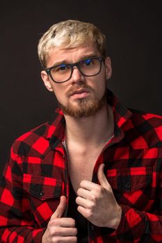 Close-up portrait of attractive young bearded hipster man wearing glasses dressed in shirt in a cage isolated over black background. Studio shot