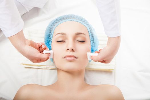 Woman with eyes closed at spa procedure made by cosmetologist. Horizontal indoors shot