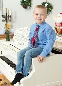 Elegant little boy in shirt and tie sitting on a white piano.In the Christmas night.