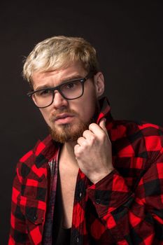 Close-up portrait of attractive young bearded hipster man wearing glasses dressed in shirt in a cage isolated over black background. Studio shot