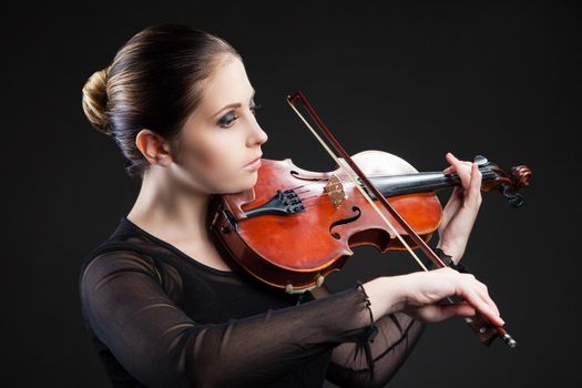 Beautiful young woman playing violin over black background