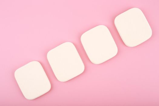 Four square shape make up sponges in a row on bright pink background. Concept of make up sponges, beauty blenders and art of visage