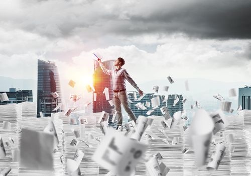 Side view of man in casual wear keeping hand with book up while standing among flying papers with cityscape and sunlight on background. Mixed media.