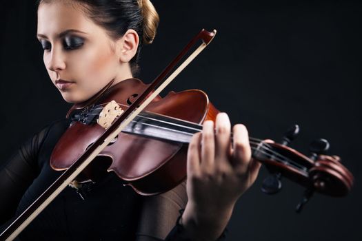 Beautiful young woman playing violin over black background