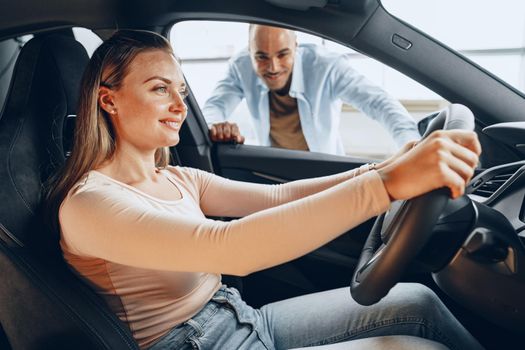 Joyful young couple looking around inside a new car they are going to buy in a car shop dealership