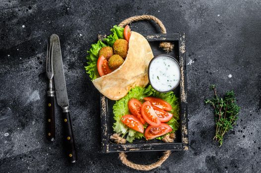 Falafel with vegetables, sauce in pita bread, vegetarian kebab sandwich. Black background. Top view.