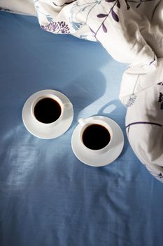 Two white cups of coffee are in bed, sunny morning.