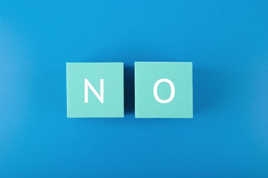 Flat lay with single word no on blue cubes against blue background. Say no to violence, toxic people, discrimination, agism and other negative factors
