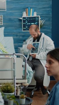 Sick aged patient looking at tablet with osteopathy x ray for diagnosis checkup in nursing home. Doctor explaining radiography scan to old ill woman for healthcare recovery treatment.