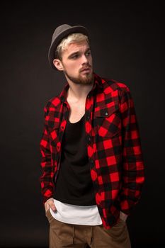 Handsome trendy young guy at the studio on black background. He wears beard and a plaid shirt. Belt portrait