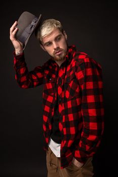 Handsome trendy young guy at the studio on black background. He wears beard and a plaid shirt. Belt portrait