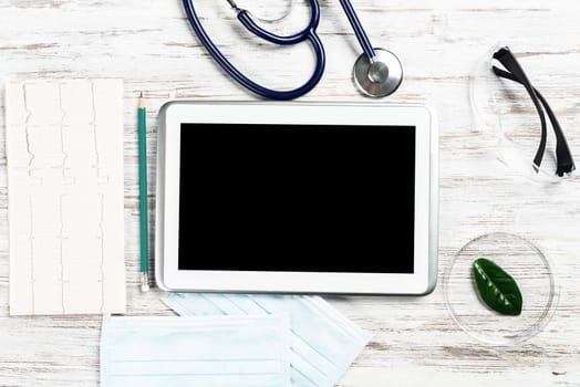 Laboratory patient examination in doctors office. Top view tablet computer, medical mask, stethoscope and cardiogram on wooden desk. Medical diagnostics and examination in modern hospital.