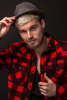 Handsome trendy young guy at the studio on black background. He wears beard and a plaid shirt. A large portrait