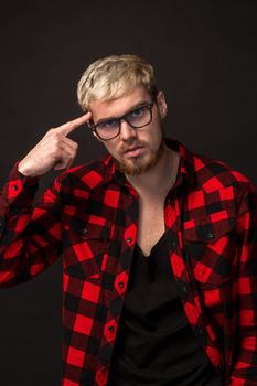 Handsome trendy young guy at the studio on black background. He wears beard and a plaid shirt. A large portrait