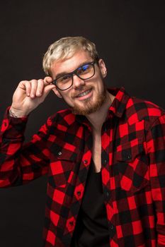 Handsome trendy young guy at the studio on black background. He wears beard and a plaid shirt. A large portrait