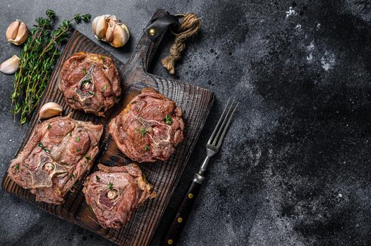 Grilled lamb neck meat steaks on a wooden board with herbs. Black background. Top view. Copy space.