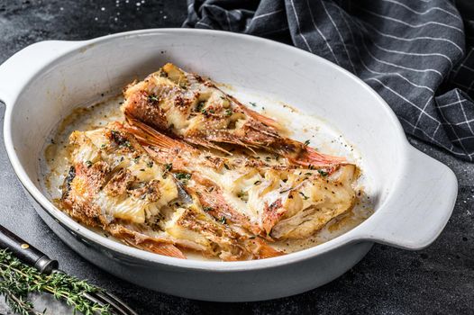 Red Sea perch or grouper baked in a baking dish. Black background. Top view.