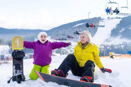 Mother and daughter with snowboards are playing in the snow