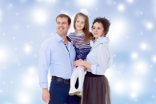 Happy young family, mom dad and little daughter.Parents keep the girl in her arms , and she hugs their neck.Blue Christmas festive background with white snowflakes.