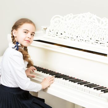 Charming little blonde with long wattled hair in plaits, playing on a white grand piano. In musical school.