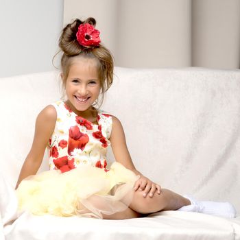 A little girl is sitting on the couch in a photo studio. Isolated on white background