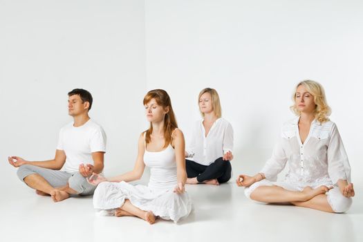 Group of people relaxing and doing yoga in white studio