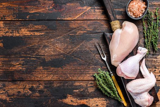 Raw chicken portions for cooking and barbecuing with skinless breasts, drumstick and wings. Dark wooden background. Top view. Copy space.