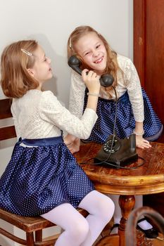 Two elegant girls sisters in beautiful dresses, talking on old phone. Retro style.Retro style.