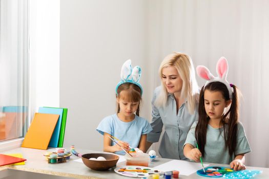 Young mother and her two little daughters painting colorful Easter eggs at home