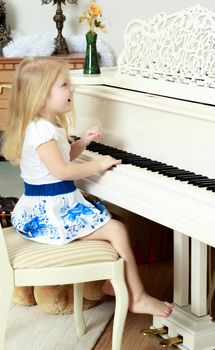 A little blonde is playing on a white grand piano.