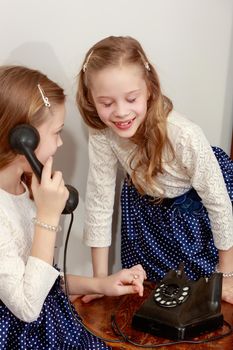 Two elegant girls sisters in beautiful dresses, talking on old phone. Retro style.Retro style.