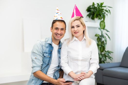 Young couple or friends in party hats having fun virtual celebration via video call.