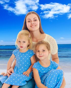 Beautiful young mother with her two daughters. Girls in the same dress with polka dots. Look directly at the camera.The concept of family happiness and mutual understanding between parents and children.