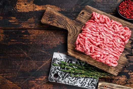 Raw mince beef, ground meat with herbs and spices on a wooden cutting board. Dark wooden background. Top view. Copy space.