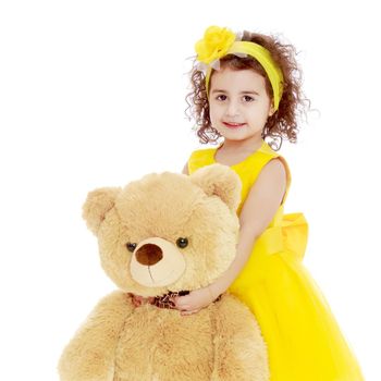 Joyful little girl Princess, dressed in a yellow dress, hugging a big Teddy bear. Standing at full height.Isolated on white background.