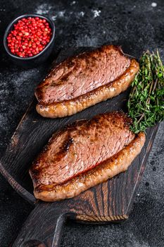 BBQ Grilled top sirloin cap or picanha steak on a wooden cutting board. Black background. Top view.