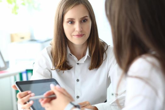 Portrait of joyful businesswoman sitting in office with friendly female manager and holding tablet in tender hands. Copy space on screen. Business meeting concept