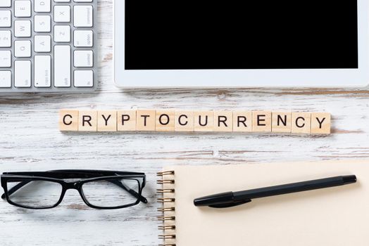 Cryptocurrency concept with letters on cubes. Blockchain technology and digital money. Still life of workplace with supplies. Flat lay vintage wooden desk with tablet computer and spiral notebook.