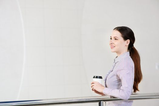young attractive woman with a paper cup of coffee, rests on railing