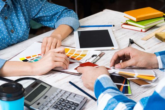 Cropped image of designer and client meeting in office. Creative workspace with color swatches and tablet computer. Interior and textile designing. Coloristics and product branding in design studio.