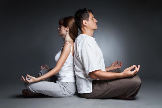 Young healthy couple in yoga position on dark background