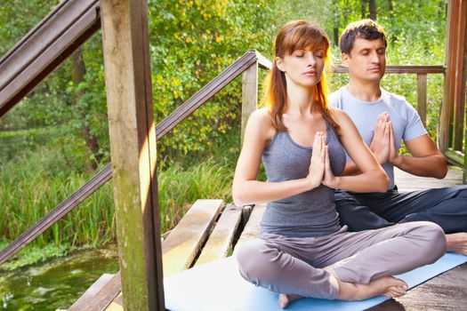 Young man and woman doing yoga. Lotus pose meditation in a garden. Outdoor full body