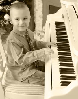 Elegant little boy in shirt and tie playing on a white Grand piano. Around the Christmas tree and the fireplace in the Christmas night.Black-and-white photos , retro style.